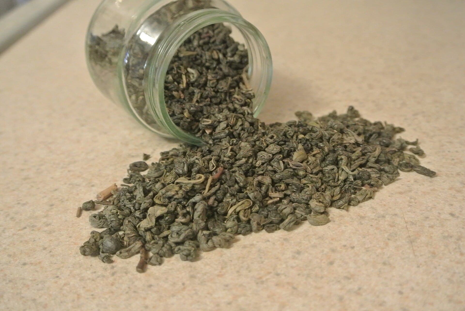 Gunpowder green tea pellets spilling from a glass jar